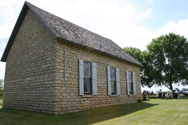 A rear view of the Old Stone Church, a simple structure with three shuttered windows running along each side of the building.