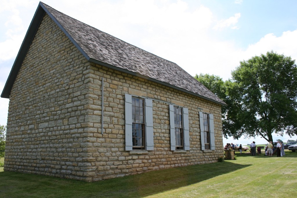 A rear view of the Old Stone Church, a simple structure with three shuttered windows running along each side of the building.