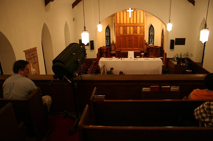 A view from the balcony before the drama begins shows the spotlight to the left and The Last Supper table below. The actors enter, spotlighted in the dark church, to take their seats at the table. There they "freeze" in place to mimic Leonardo da Vinci's painting.