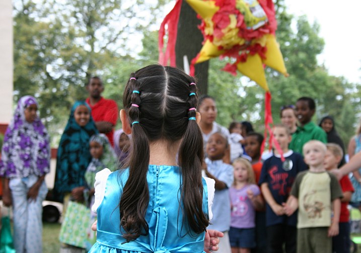 A little girl stands on the opposite side of the group of children waiting to swing at the pinata.
