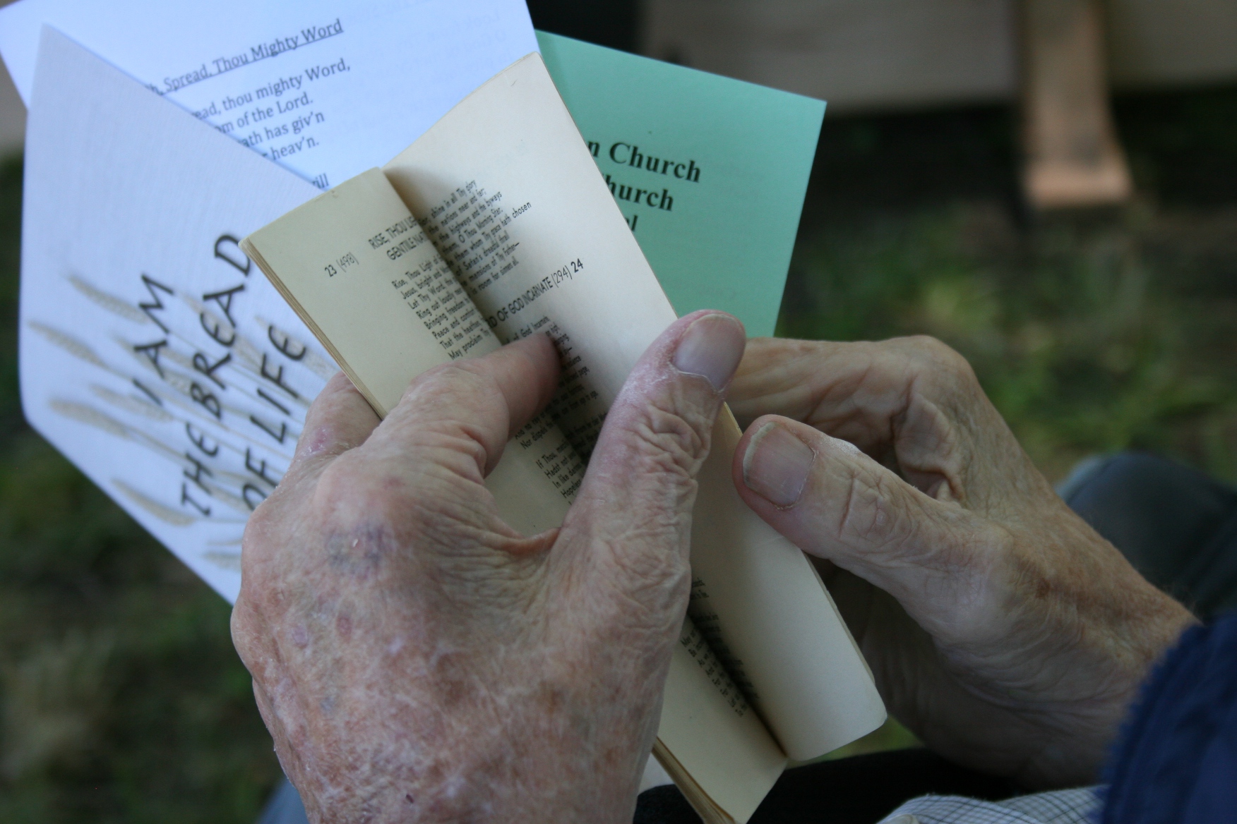 An elderly man turns to a hymn in the old pocket-size songbook that's been used for decades.