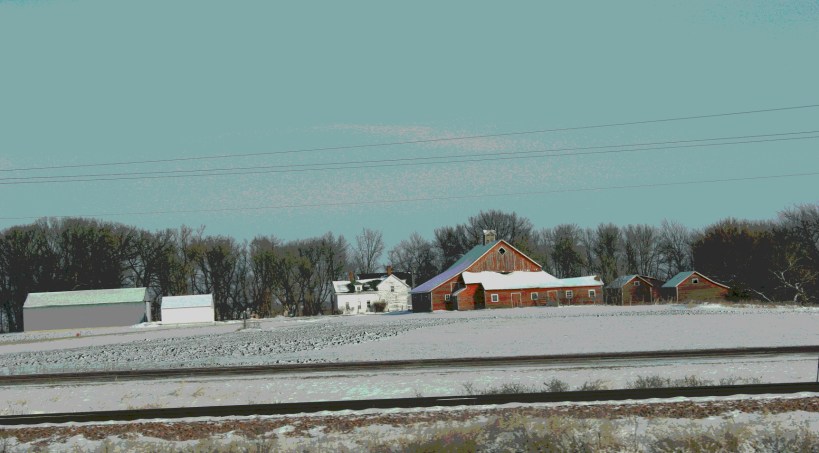 The horizontal lines of railroad tracks and farm buildings define this scene near Janesville along U.S. Highway 14.