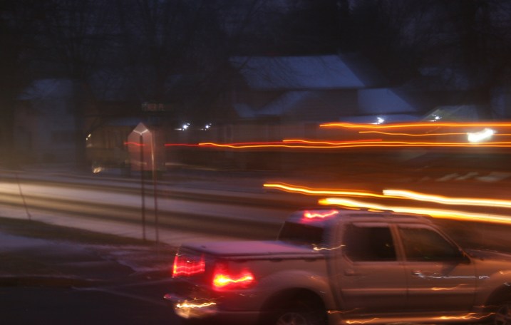 The blurred lines of a school bus passing by as a pickup waits on a side street.