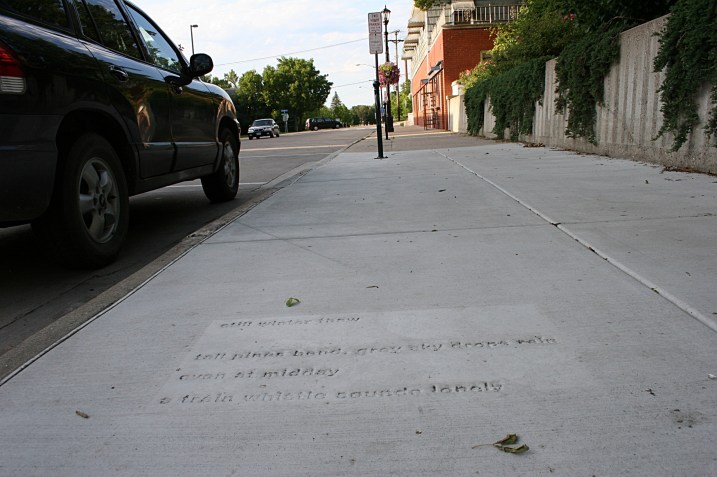 A poem by Patrick Ganey is stamped into the sidewalk near the Northfield Public Library. It reads: still winter thaw  tall pines bend, grey sky drops rain  even at midday  a train whistle sounds lonely