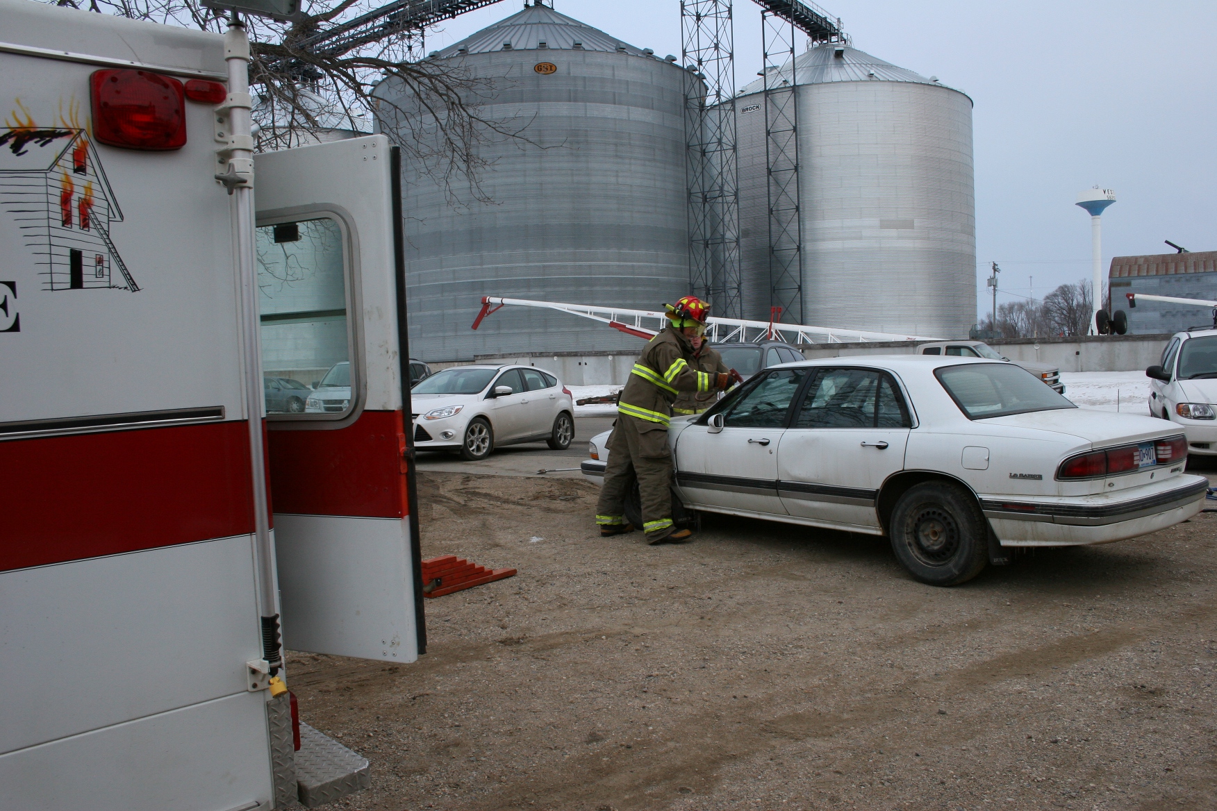 Volunteer firemen remove the windshield from a junk car.