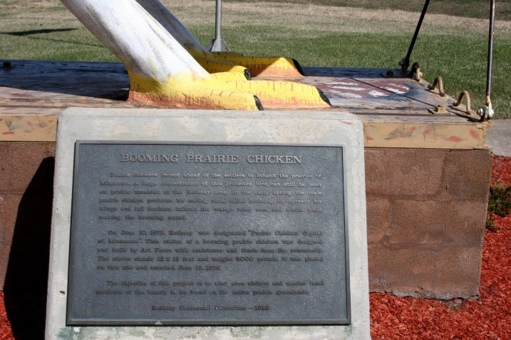 The feet of the giant prairie chicken along with info about the statue built in 1976 by artist