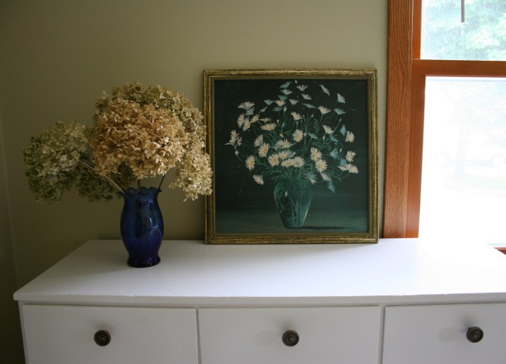 In the guest bedroom, I created this floral scene atop a dresser. The floral print came from a garage sale, bought for under $1. I seldom spend much on any art I buy. The hydrangea are from my frontyard bush and the vase from flowers I once received.