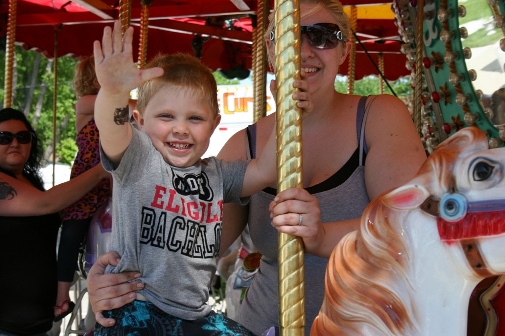 Dakota waves to his dad who is photographing his little boy's ride on the merry-go-round.