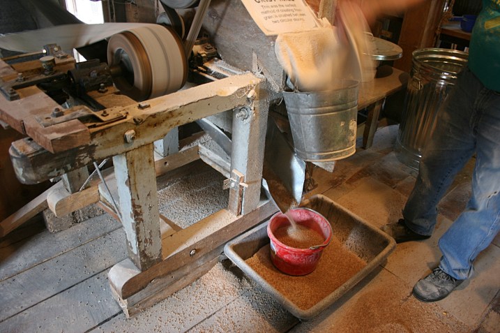 A volunteer grinds wheat into flour in the old grist mill. Each time the waterwheel turns, it spins the millstone 17 times in the process of crushing grain between stones. The volunteer's wife bakes Communion bread for the local Methodist church.