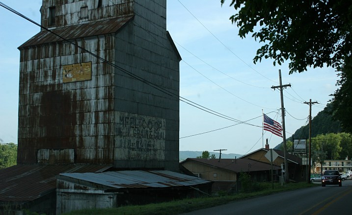 Snapped through the windshield of the van, this aged elevator and flag to the right, entering the Mississippi River town of Marquette, Iowa, from the north.