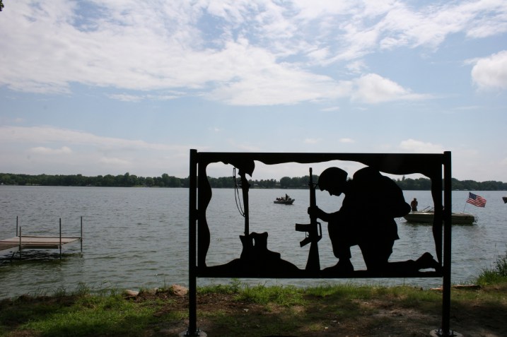 The "Window in Time" memorial shows a current day Marine praying before a grave/memorial. The young man depicted in the 4x8-foot steel sculpture is carrying a heavy burden, Kirk Mansfield notes, with the burden on his back representing a simple thank you. The tipped helmet also symbolizes thanks. The weapons are representative of those from WW II and the Korean War. The piece carries a theme of honoring and respecting elders. Mansfield was joined by many volunteers in working on the project.