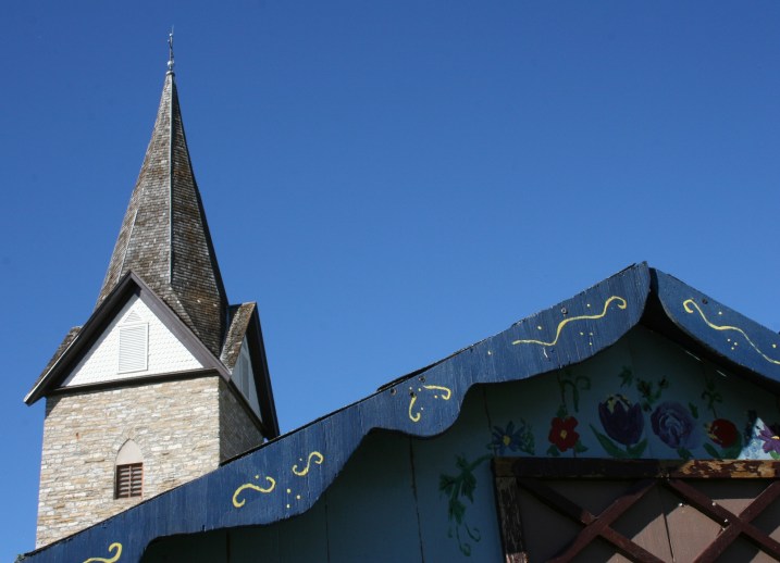The steeple of the historic stone church with the roofline of a German themed beverage booth in the foreground.