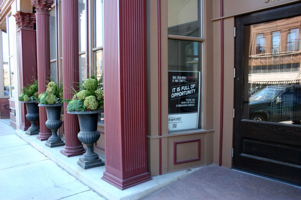 The historic Bachrach Building in downtown Faribault was the perfect venue for the wedding couple's vision of their reception. However, about a month before the wedding, I noticed that the flowers in the outside urns were mostly dead or dying. When I mentioned this to Amber, she admonished me to drop the idea of replacing the flowers because she did not want to spend more time and money on this. Because first impressions count, I contacted my floral designer sister. Together we hatched a no-cost easy plan to beautify the urns. I clipped nearly 40 hydrangea from my yard. Lanae brought ornamental kale, curly willow and greens from hers. She transformed the urns into stunning floral masterpieces that impress.
