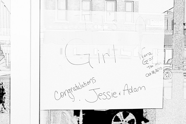 A birth announcement in the front window of a downtown business, converted to black-and-white so it's readable.
