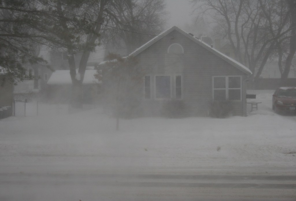 A view from my front window around 4:30 p.m. shows reduced visibility due to blowing snow and fresh snow falling.