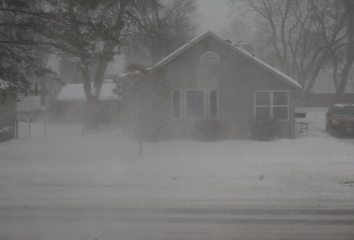 A view from my front window around 4:30 p.m. shows reduced visibility due to blowing snow and fresh snow falling.