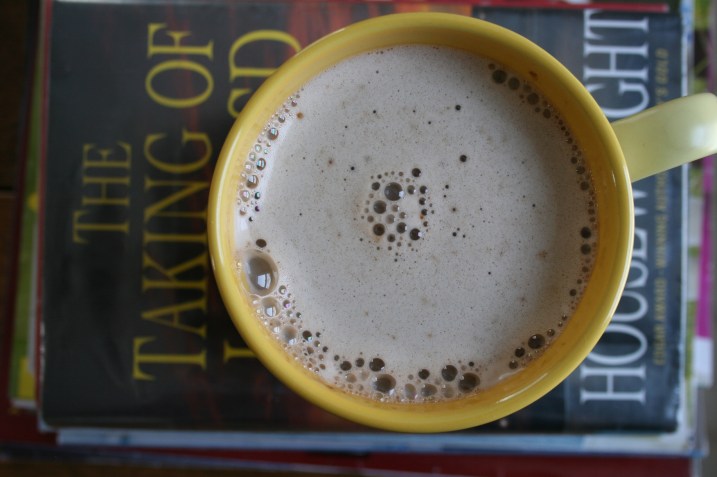 A cup of instant cappuccino set atop a stash of books.
