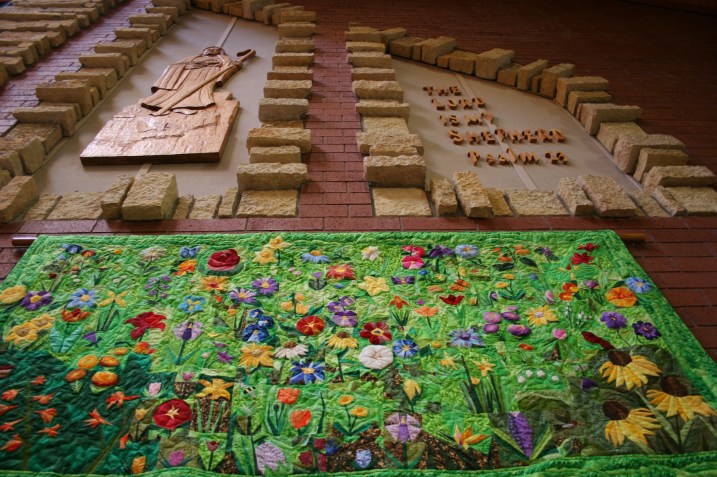 The beautiful and stunning floral quilt art by Kevin Kreger is displayed below a wood carving by noted Faribault artist Ivan Whillock. Kreger coordinated the "Consider the Lilies" floral display at Trinity.