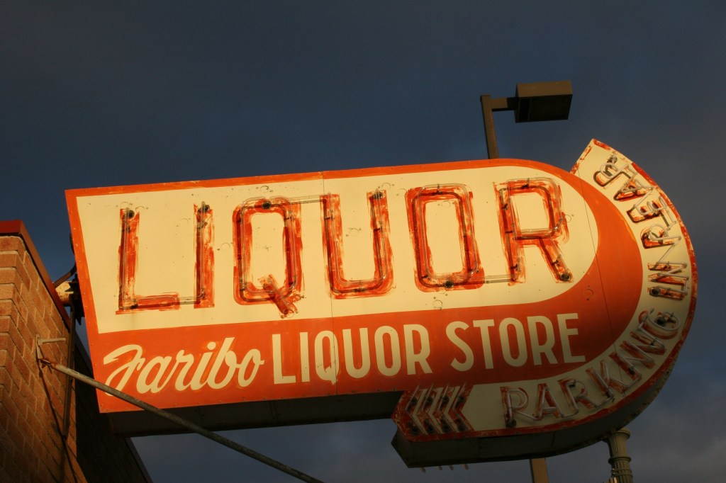 The setting sun spotlights vintage Faribo Liquor Store signage along Fourth Street/Minnesota Highway 60 in downtown Faribault. Minnesota Prairie Roots file photo 2009.
