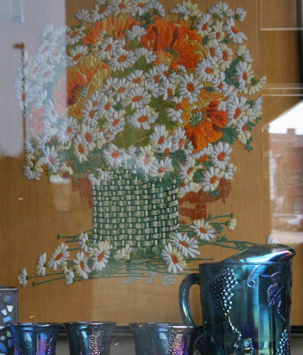 This crewel embroidery art, crafted by the same woman who created the floral I purchased, now hangs in the front window of the Nook & Cranny.