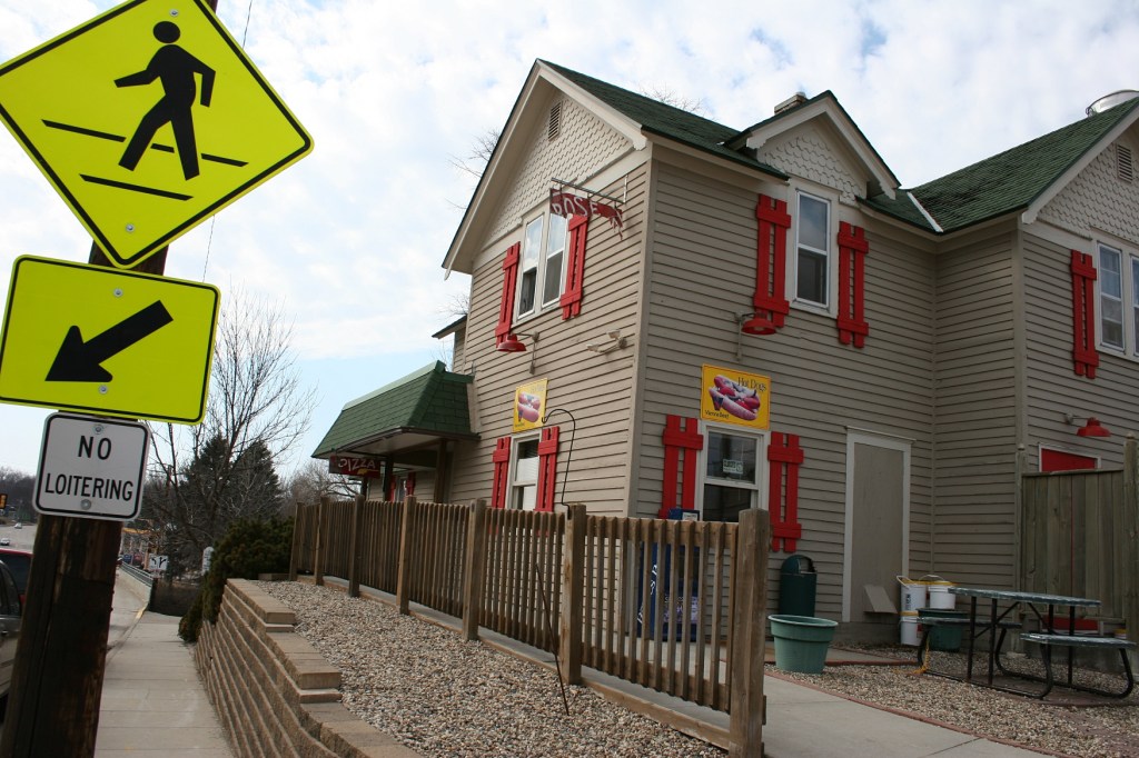 The building that houses the ice cream shop and a pizza place. Lots of loitering going on down the sidewalk and to the right at the walk-up ice cream window order area and  patio.
