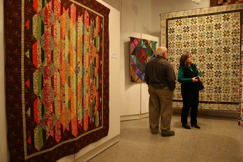 The quilter's husband and the quilter view the extensive collection of quilts.