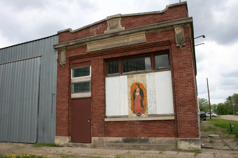 The front window of the 1910 Delhi State Bank is now mostly boarded with a painting of Our Lady of Guadalupe.