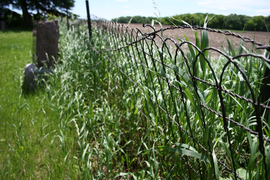 A fence separates graveyard from fields.