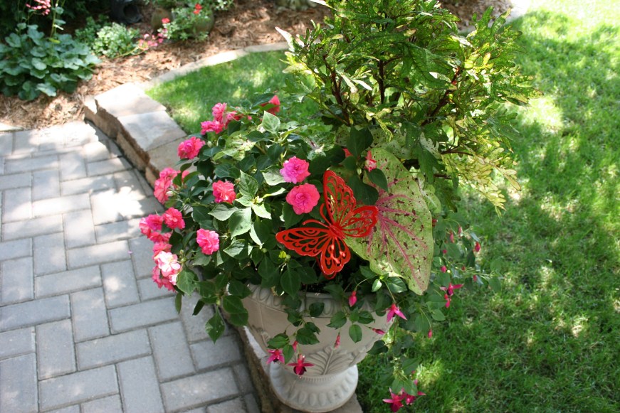 Impatiens and butterfly art add color to a plant situated along a walk way.