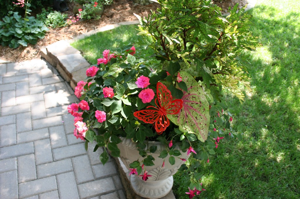 Impatiens and butterfly art add color to a plant situated along a walk way.