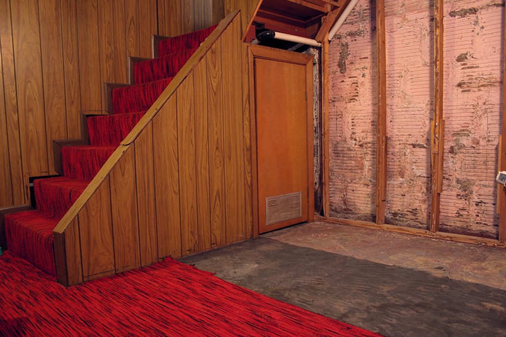 Gutting of our basement is well under way. This photo shows paneling stripped from the clay tile foundation walls with some paneling remaining yet on along the stairway. The floor shows carpet backing scraped off, backing to be scraped off and the not-so-lovely carpet.