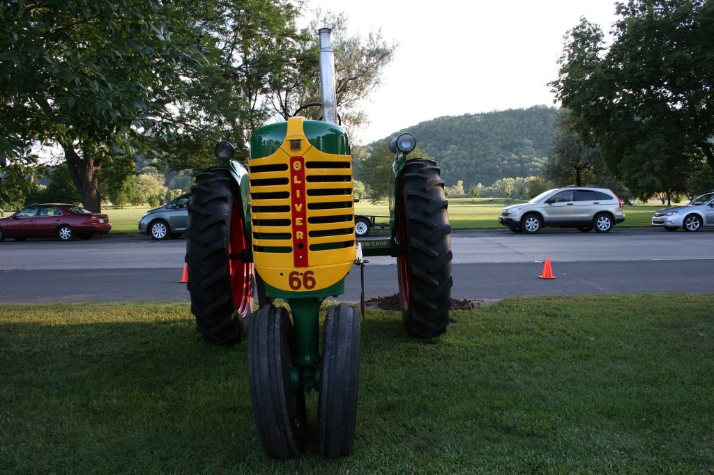 A lovely old Oliver parked on the edge of the parking lot across the street from a spacious city park.