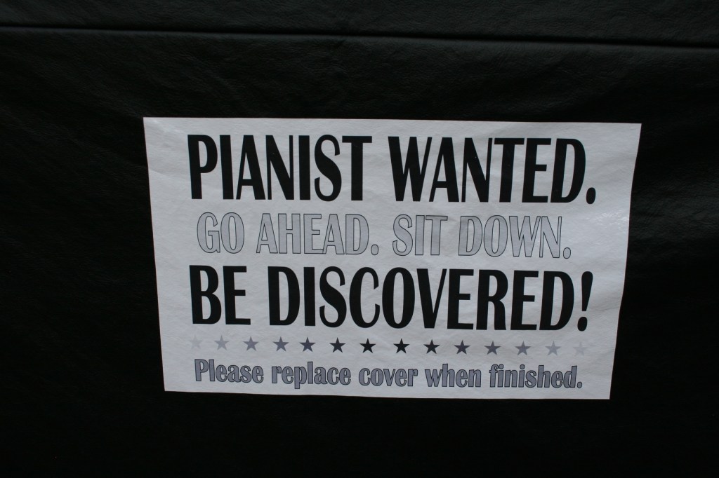 A sign invites pianists to sit down and play.