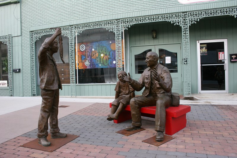 Sculptor Martha Pettigrew's "Fish Story," featuring a grandfather and two of his grandchildren, has been purchased as a permanent part of the city's sculpture collection. The red bench was recently replaced by a gray bench.