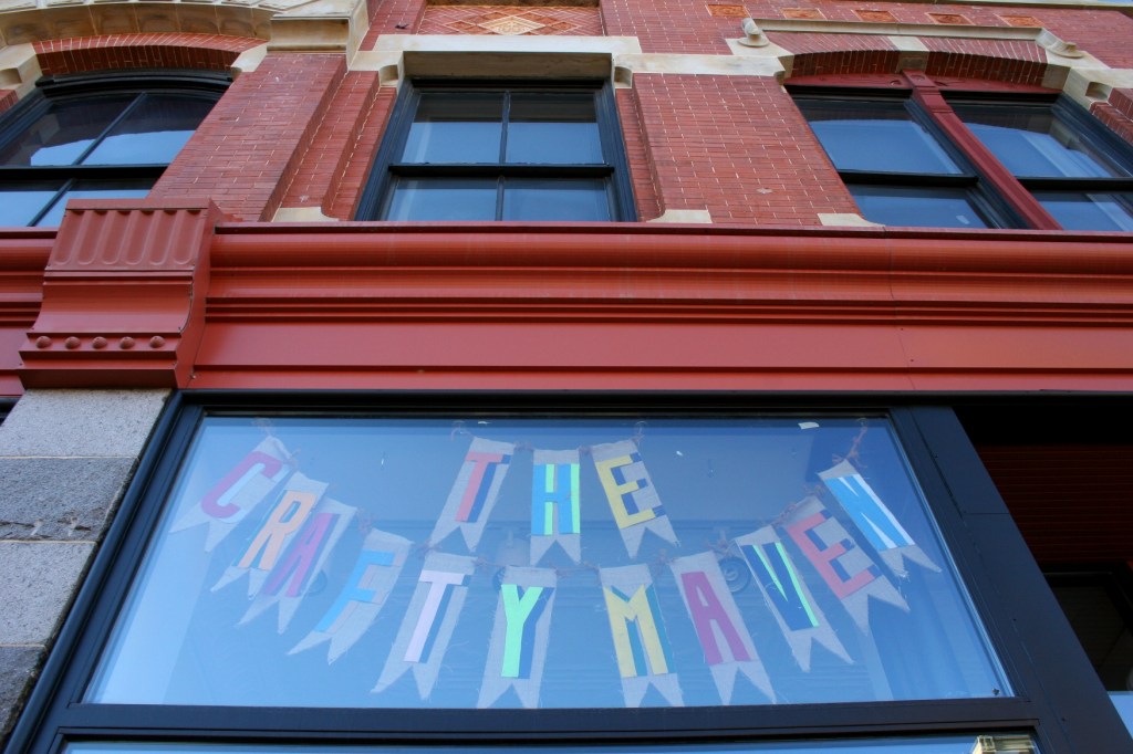 Crafty signage suspended high in a window at The Crafty Maven hints at the crafty goodness you will find inside this historic building at
