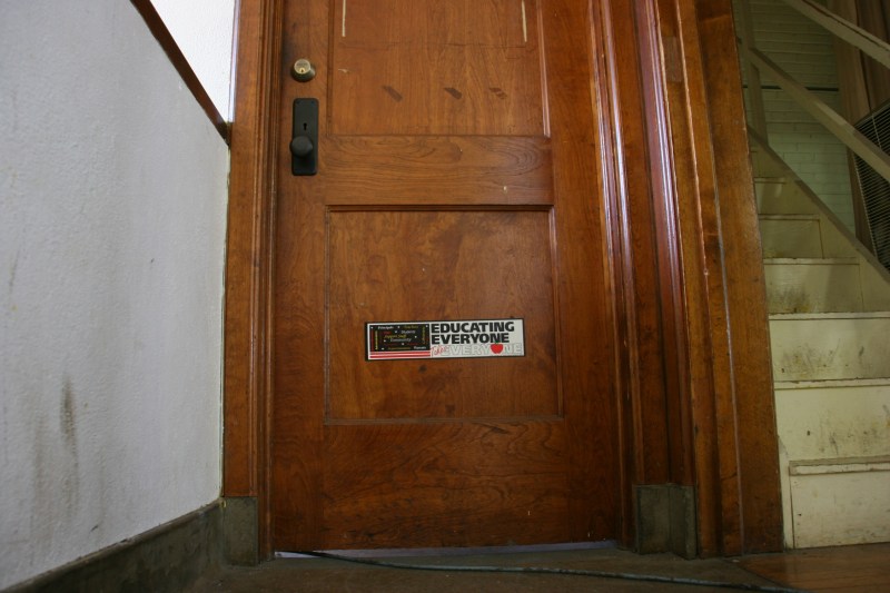 A sticker, "Educating Everyone Takes Everyone," on a sturdy wood door reminds visitors of this structure's original purpose.