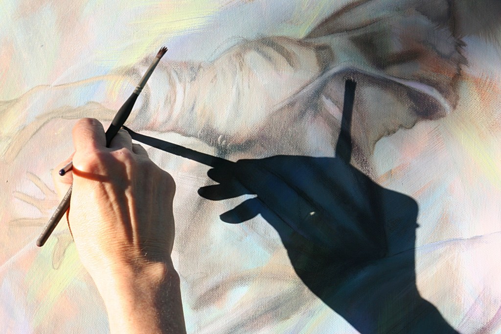 The sun shadows Dana's hand across her art as she paints.