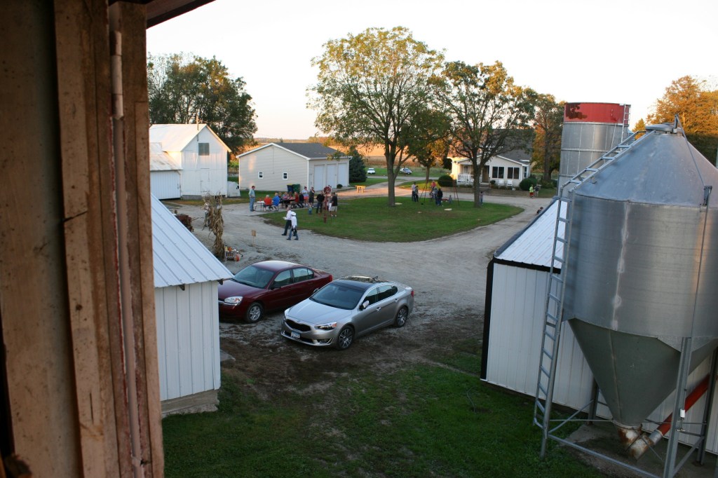 A view of the farmyard and barn dance guests from a hayloft window.