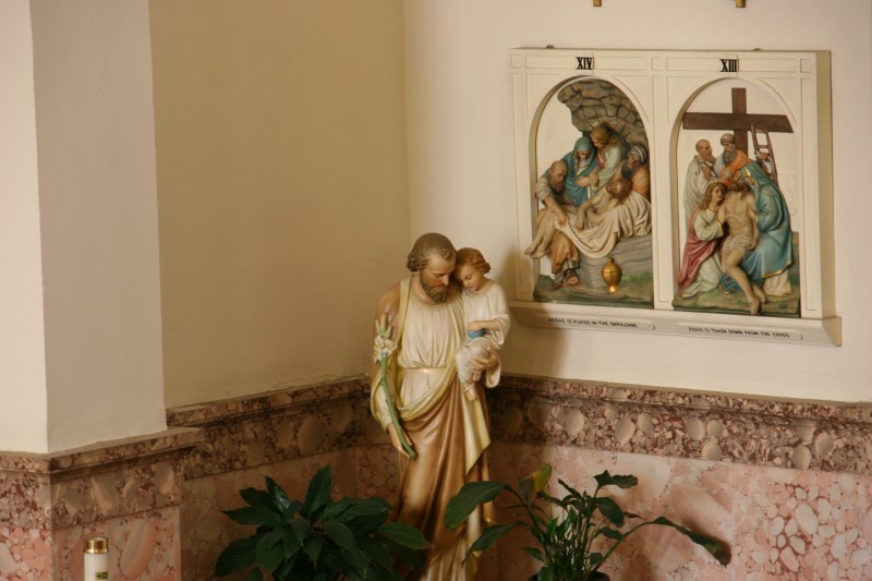 A statue is tucked into a corner below stations of the cross.