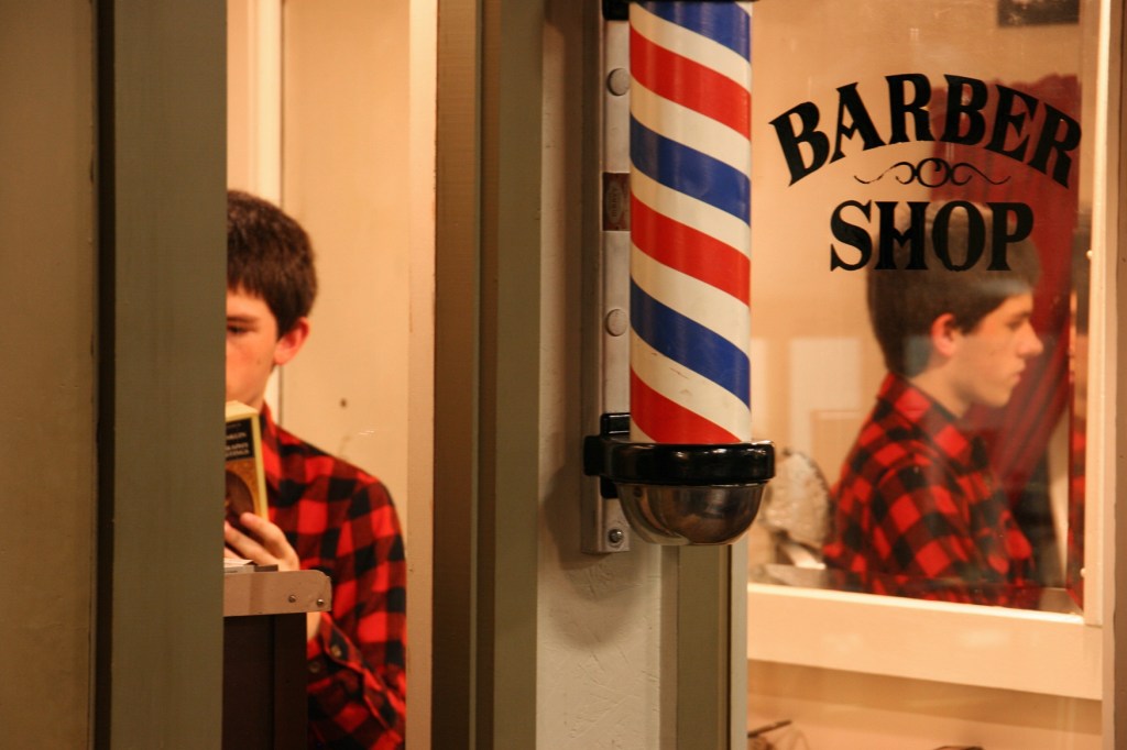 A high school reenactor reads a book in the museum barbershop.