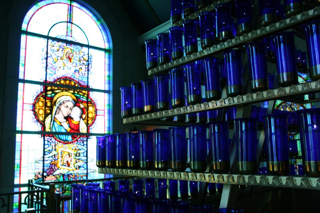 A rack holds 576 candles inside the Mother of Good Counsel Votive Chapel. Pilgrims, for a price, may have a candle lit. A lift allows lighting of the tiered candles stretching high into the chapel.