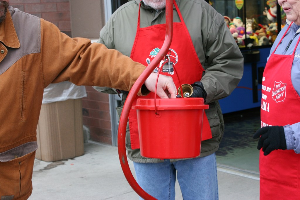 A man drops coins into the red kettle tended by Bud and Bev.