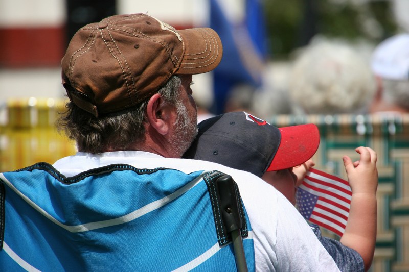 Nestled on his grandpa's lap, this young boy holds an American flag.