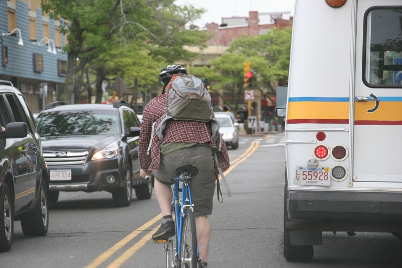 A biker squeezes around a bus in busy Davis Square.