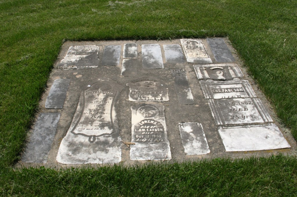 Aged tombstones, which I assume once stood vertically, are now cemented flat into the ground.
