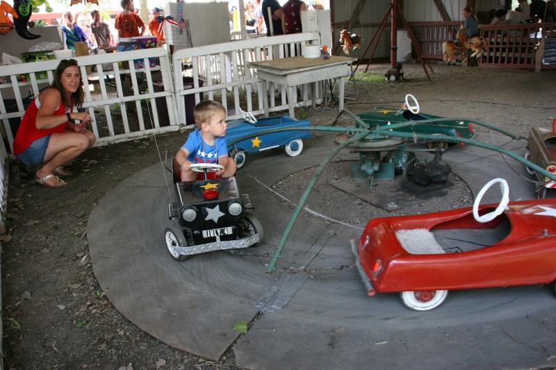 Cooper rides a vintage car while his mom watches.