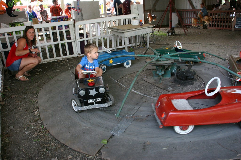 Cooper rides a vintage car while his mom watches.