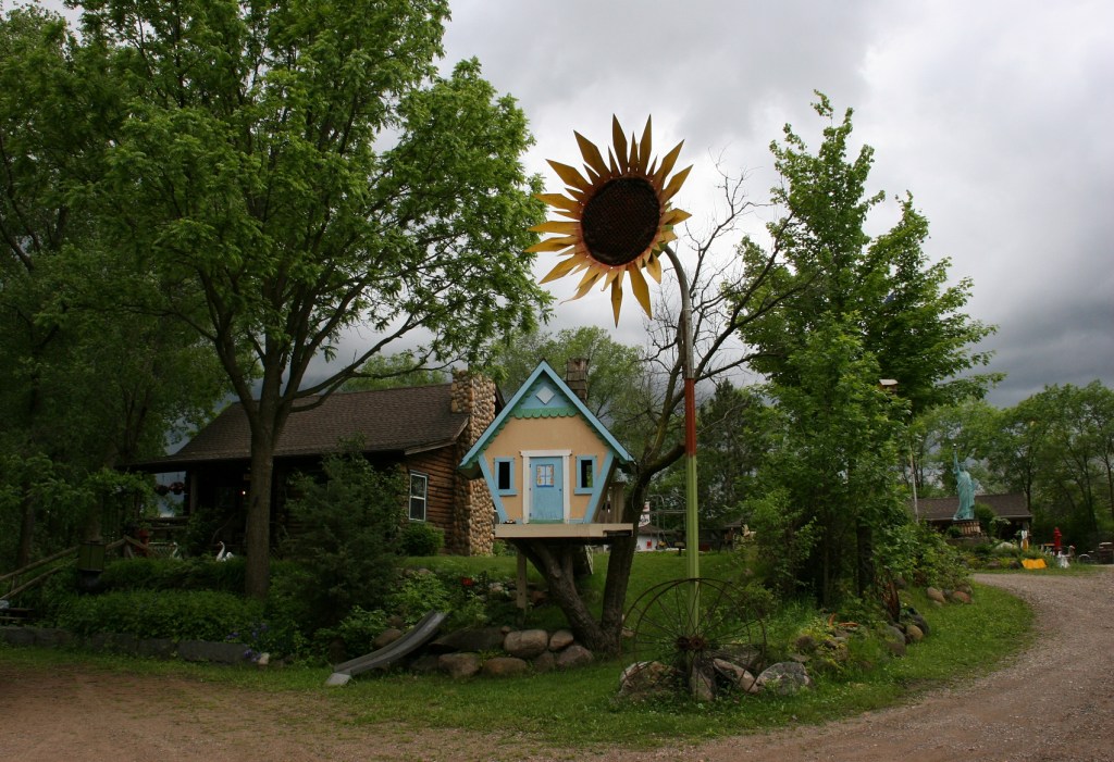 Behind the sunflower and the fanciful treehouse are a log cabin and other buildings housing antiques for sale.