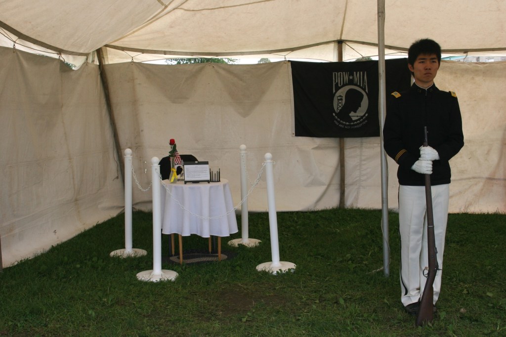 Inside a tent reserved for remembering those missing in action and those who were prisoners of war, a member of the Shattuck-St. Mary's School Crack Squad stands at rigid attention.