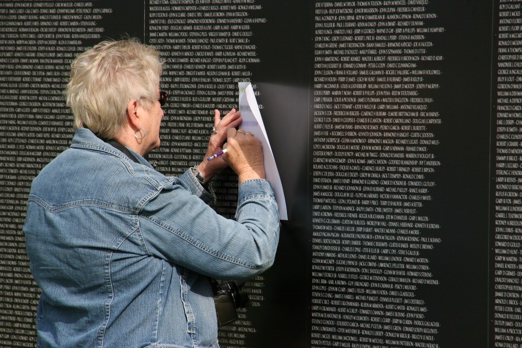 A woman does rubbings of names on the wall.